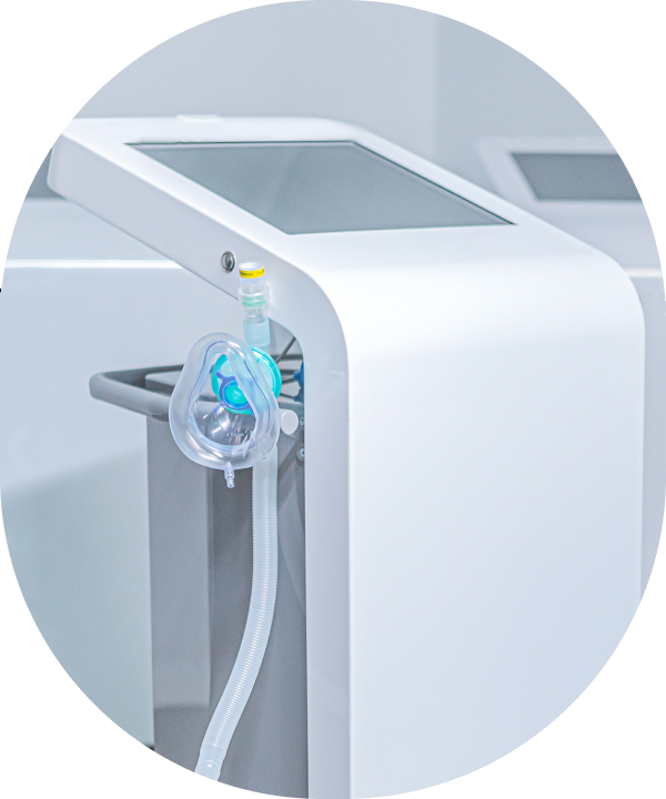 Close detail of the treatment console: a white cabinet with a dark touchscreen at the top and a clear soft mask hanging on a ribbed hose at the side.