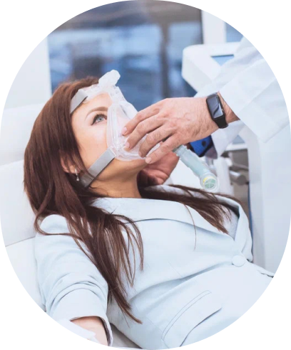 A clinician fits a soft breathing mask to a woman reclining in a treatment chair.